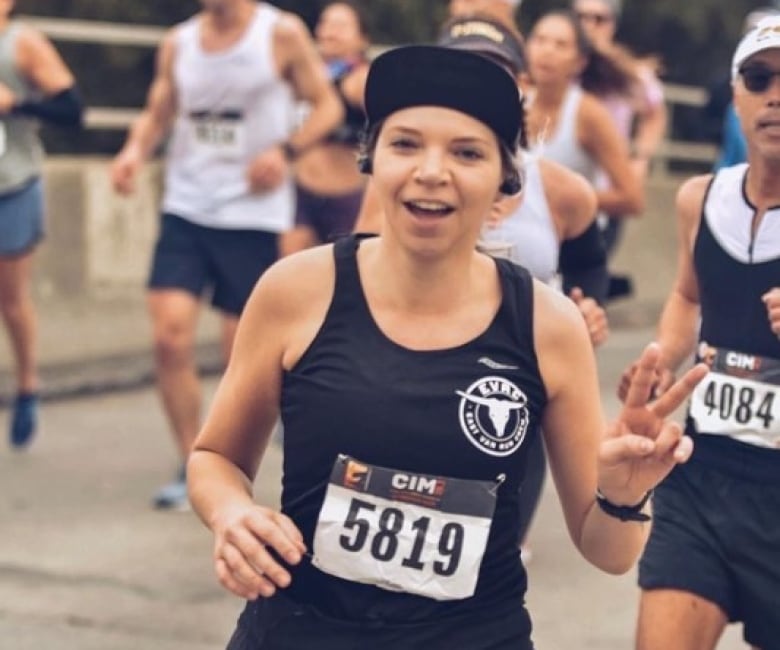 A young white woman in a black vest running in an organized race.