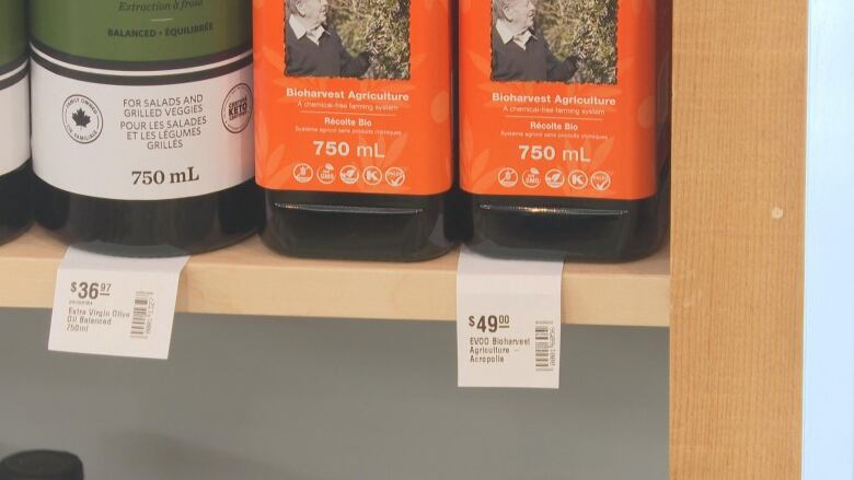 Bottles of olive oil on the shelf showing tags of $36.97 and $49.00