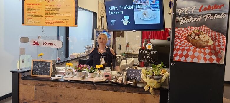 A woman stands behind the counter of a decorated cafe/resturaunt counter.