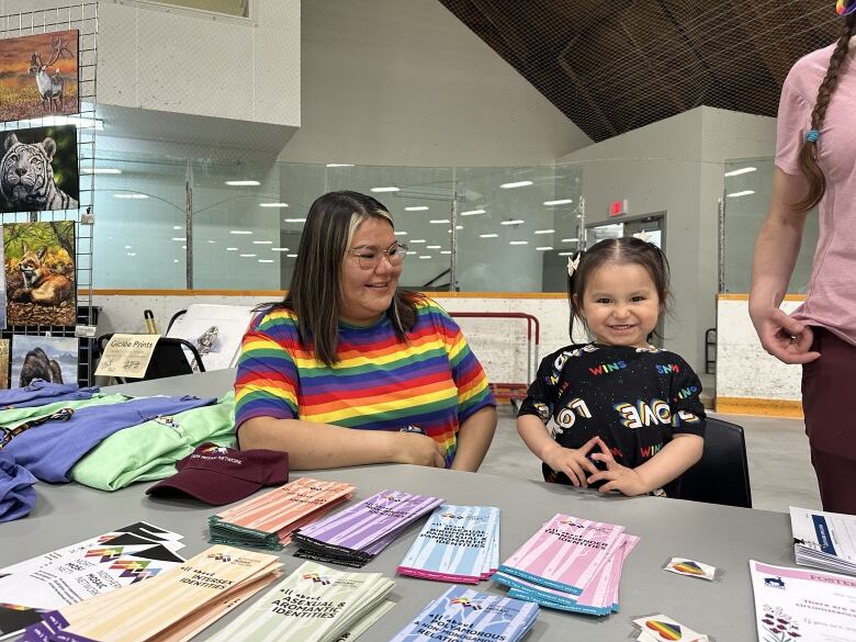 A woman in a rainbow striped sweater smiles at a child in a shirt that says 