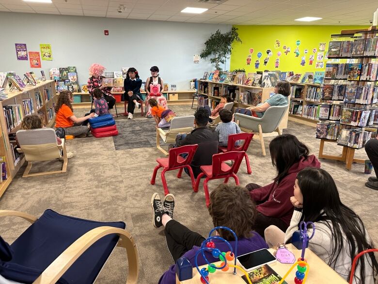 A bunch of people sit in a library listening to someone read a book.