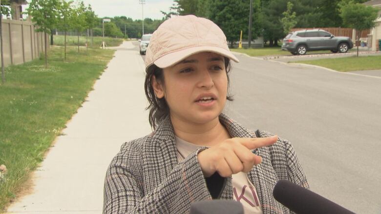 A woman in a beige cap speaks and points.