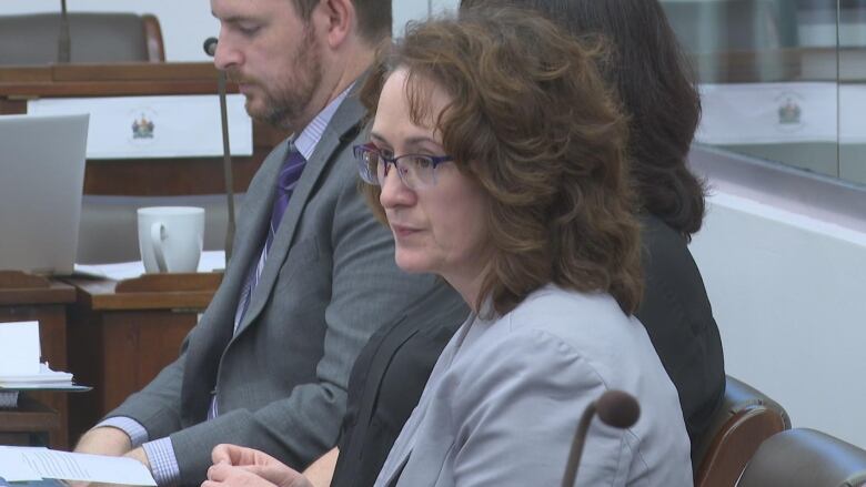 A woman in a suit sits at a committee. 