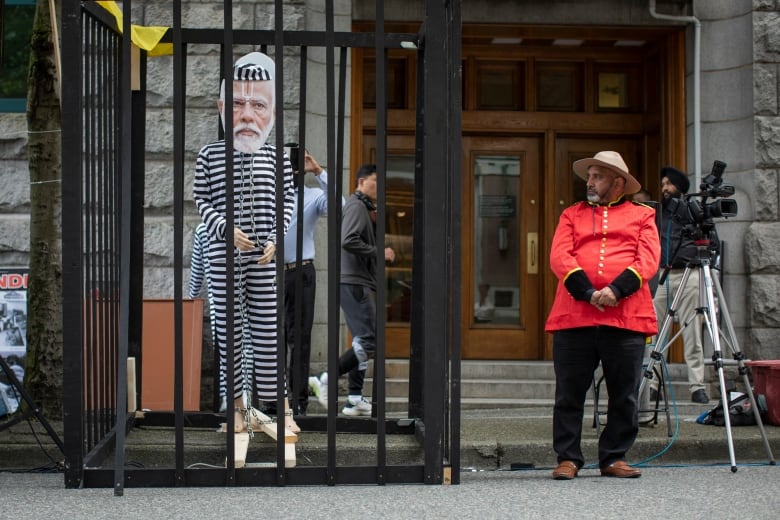 An effigy of a man in prison clothes i s seen in a prop jail cell, with a person wearing red Mountie clothes looking at it.