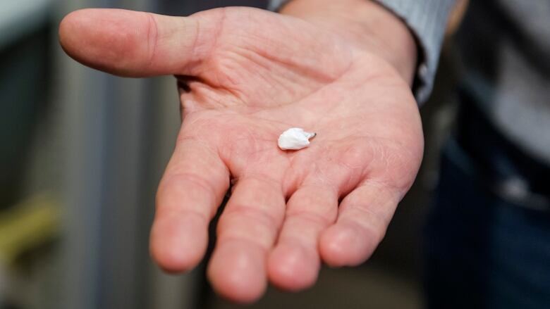 A man holds a small baggie with a tiny white powder inside.