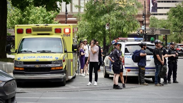 an ambulance, police and onlookers gather in a city square