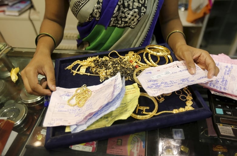 A salesperson's arms and hands are seen as they display gold jewelry.