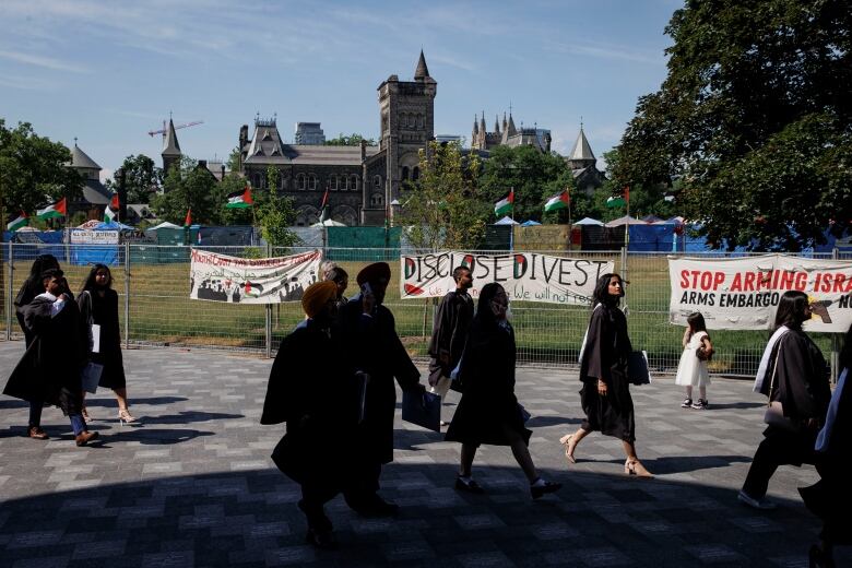 University of Toronto graduates exit a convocation ceremony, with an on-going pro-Palestinian encampment in the background, at the colleges downtown campus on June 4, 2024.