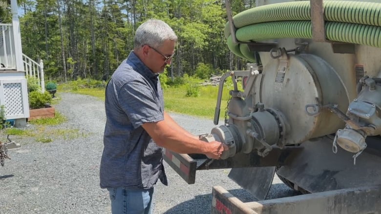 A man in short sleeves makes adjustments to a valve at the back of a sewage hauling truck.