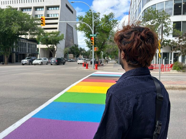 A man standing in front of a rainbow crosswalk with his back seen.