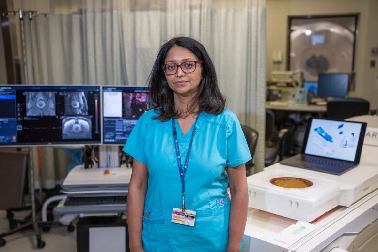 Woman in scrubs stands in hospital in front of an high intensity focused ultrasound machine. 