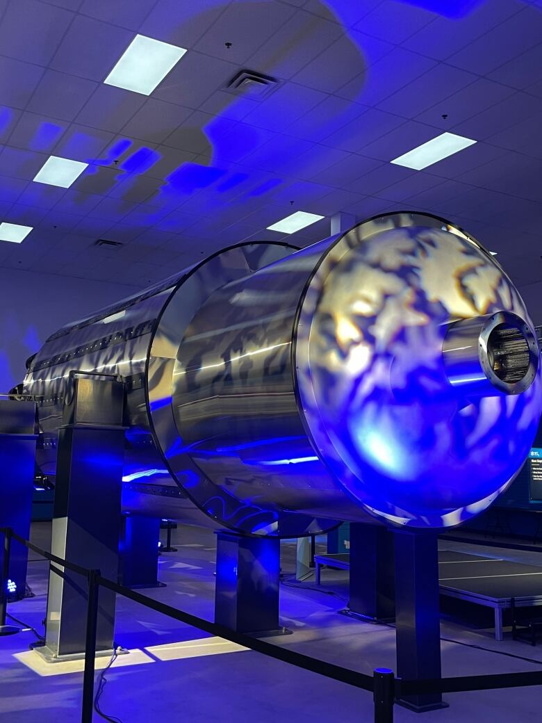 A large cylinder is on display in a darkly lit room. 