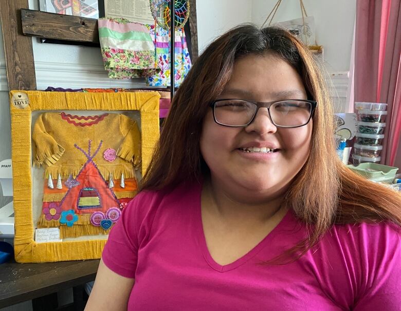 A girl sits with a big smile in front of an art piece.