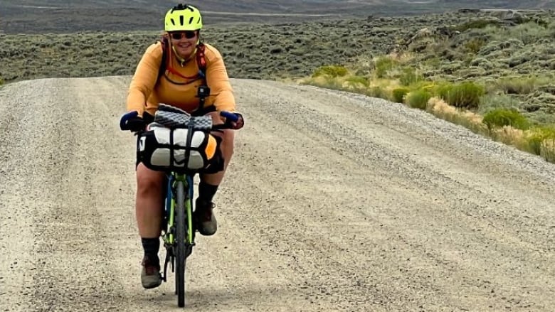 A woman rides up a hill on a gravel road.