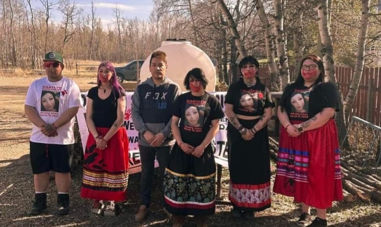 A group of people wear shirts with a woman's photo and a face paint of a red hand across their mouths, symbolizing missing and murdered Indigenous women in Canada and the United States.