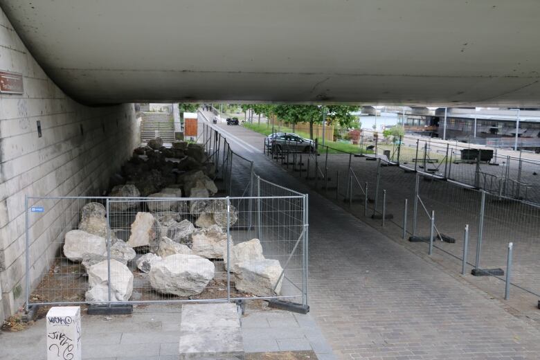 Rocks line a path under a bridge. A grey fence has been placed around it.