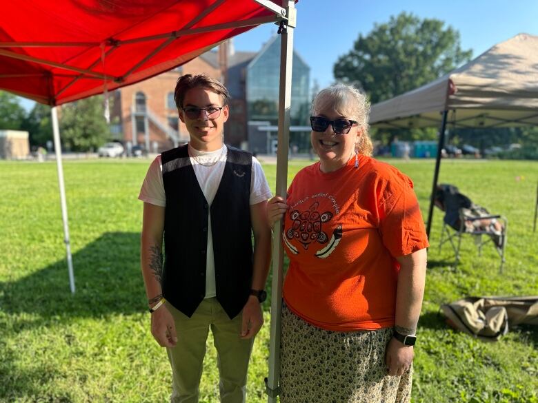 a woman wearing an orange every child matters shirt and her son stand in the sunshine. 