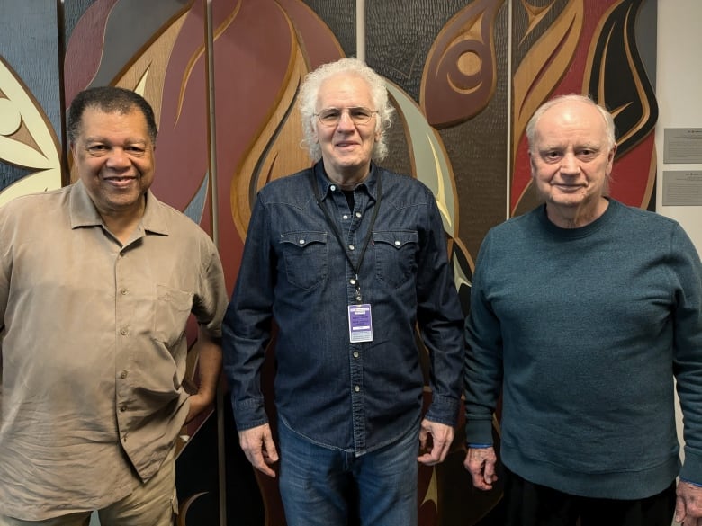 Three older men stand smiling into the camera.