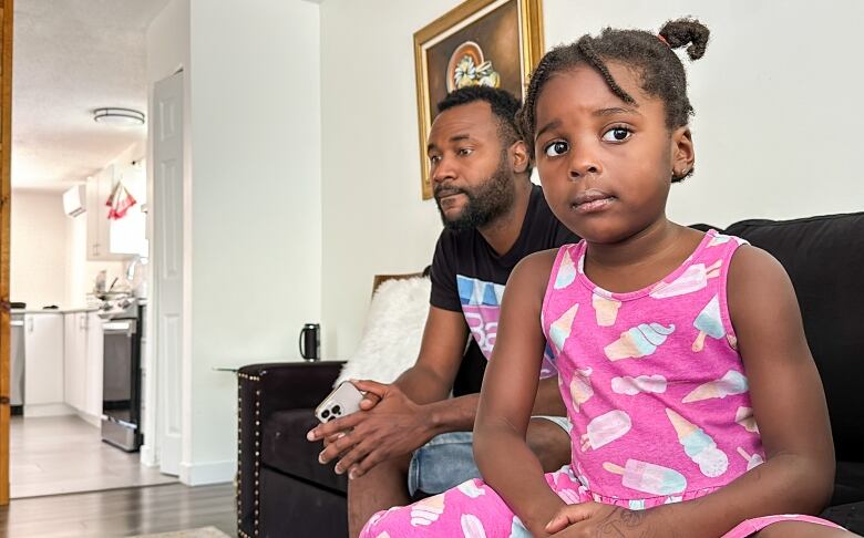 A man sitting with his young daughter on a couch. 