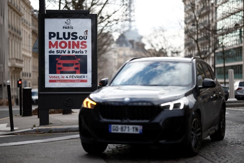 A car drives past a sign on a Paris street asking if there should be more or fewer SUVs.