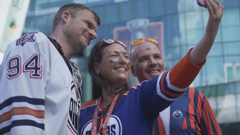 Three people wearing hockey jerseys are standing together outside, smiling while taking a selfie.