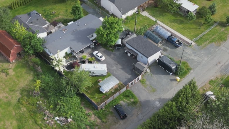 An aerial image of a house surrounded by green fields, with cars and trucks visible.