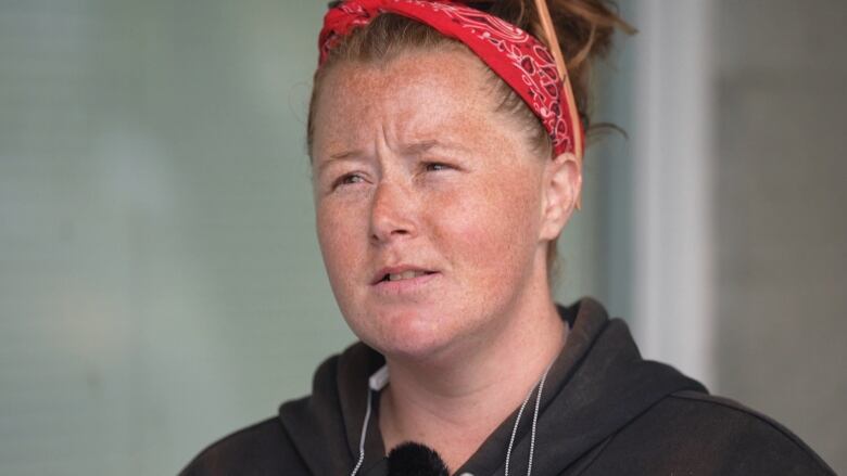 A woman with a red bandana and a black hoodie on speaks.