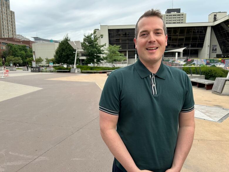 A man in a green polo shirt stands in a university square.