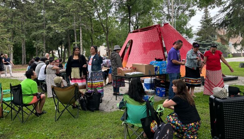 People gathered in a park sitting on lawn chairs and talking near a red and orange gradient monument. 