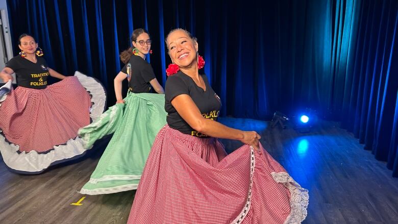 Three women in long skirts dance and turn around a room.