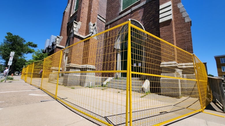 A brick churech fascade is seen through a yelow safety fence.