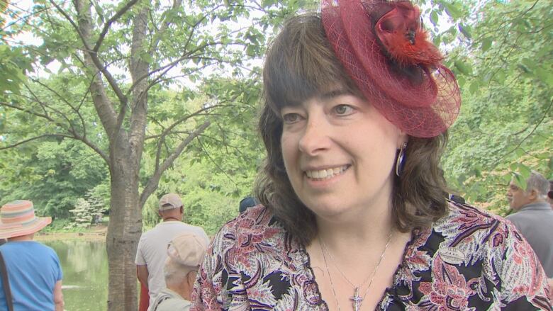 A woman wearing a pburgundy fascinator speaks to the camera