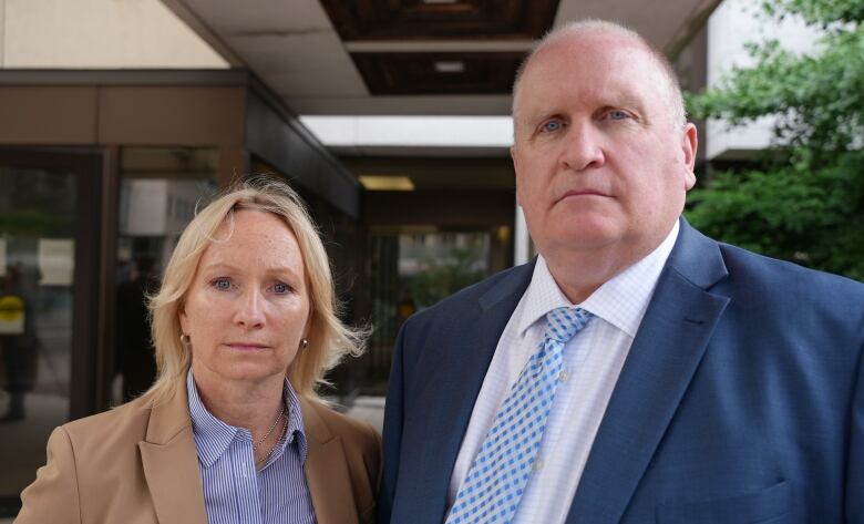 A man and a woman stand next to each other with stern faces.