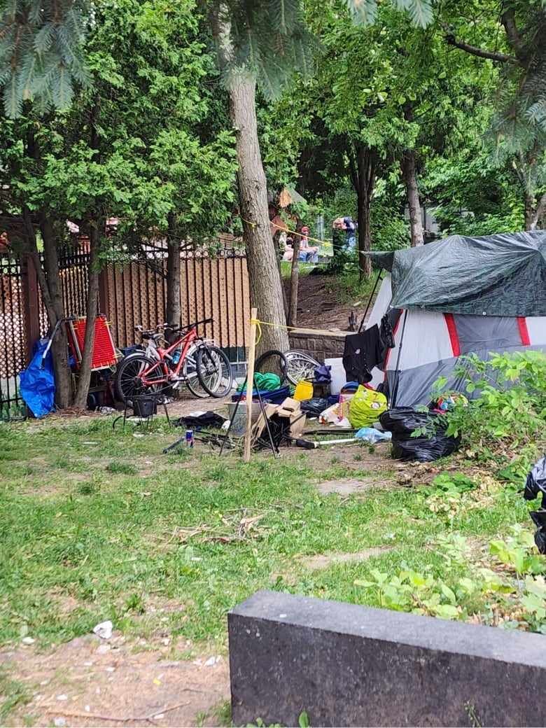 A tent is set up near some trees with bags and personal items on the ground around the tent.