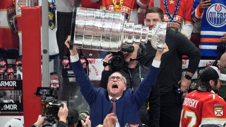 A man in a blue suit holds up a silver trophy