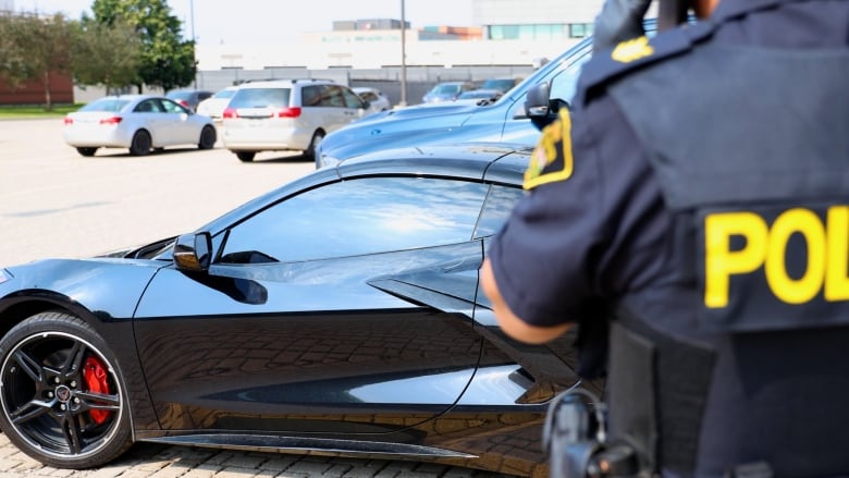 A police officer stands in front of a sports car in a parking lot.