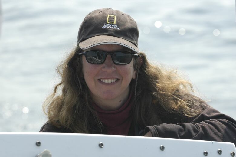 A smiling woman wearing a National Geographic hat and black sunglasses