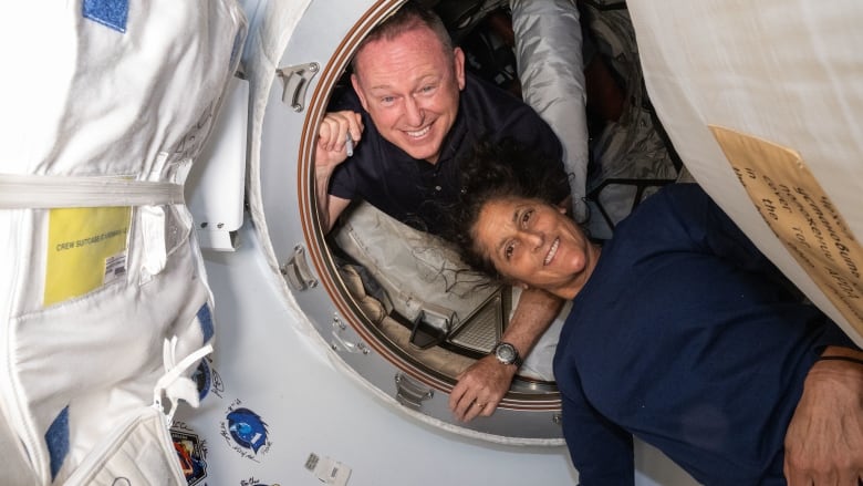 A man and a woman float in a spacecraft with big smiles.