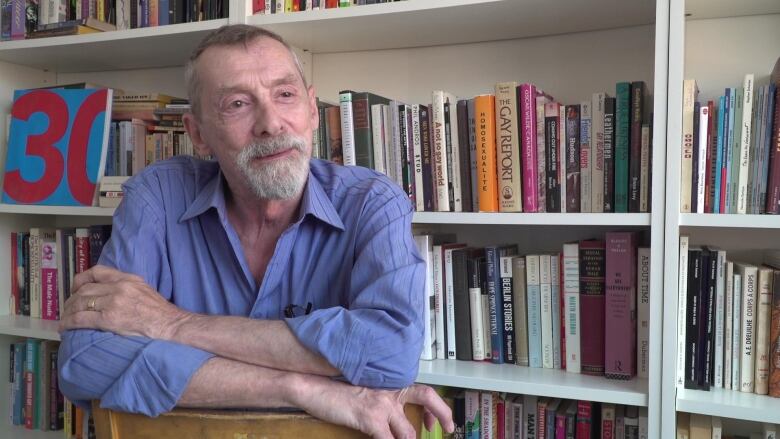 A man sitting with his arms crossed on a chair around books. 