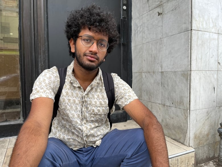 A man with curly dark hair sits on a stoop.