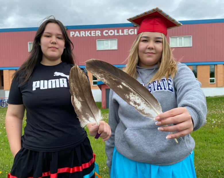 Two women hold eagle feathers close to the camera, all deadly like. 