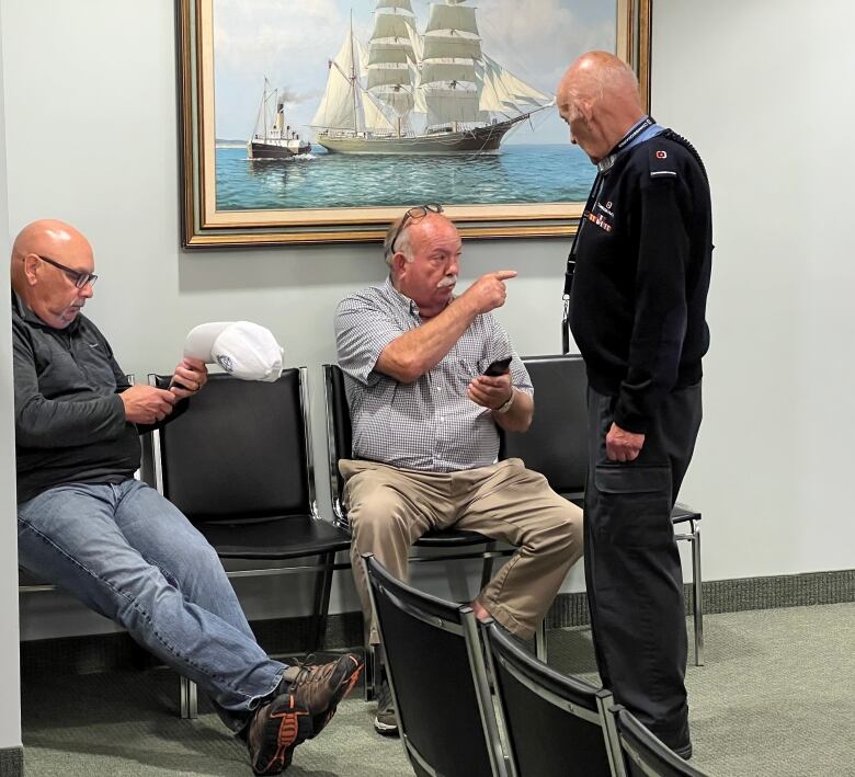 Man sitting in a chair points his finger to the right.