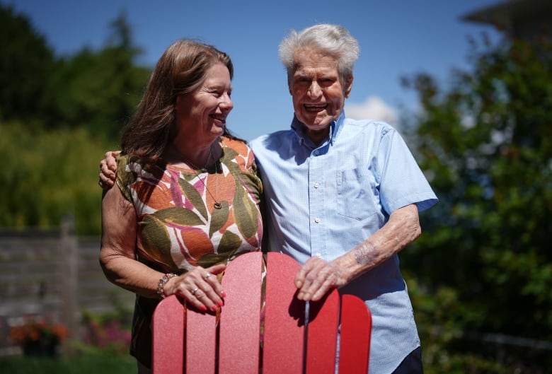 Bill Hamill, 100, poses daughter Mary Lou Hamill at their home in Gibsons, B.C. Hamill is an older white man wearing a blue shirt, while his daughter is wearing a patterned top and smiling.