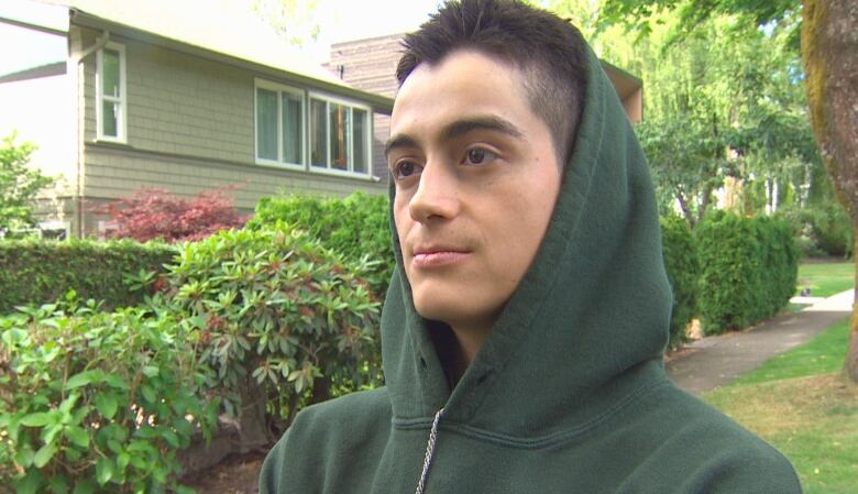 A young man in a hoodie stands in a suburban street.