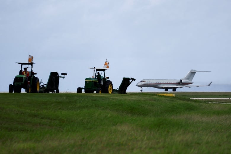 A jet is seen on a runway with two tractors in the foreground.