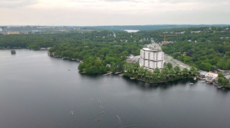 People in kayaks can be seen from above paddling down the lake, with a large grey and white building rising above the trees to their right