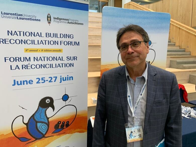 A man in a blue suit stands in front of a National Building Reconciliation Forum banner