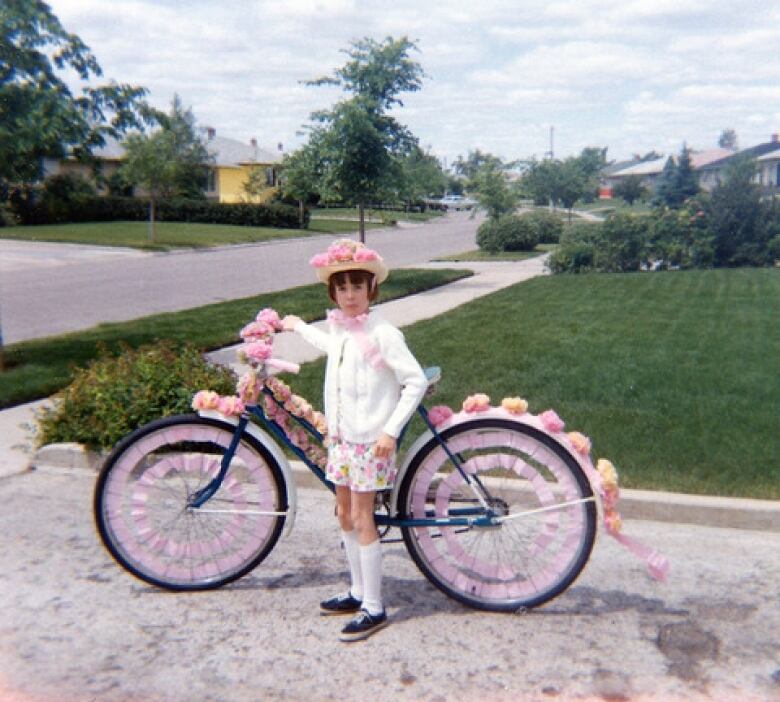 A girl of about 10 stands next to a bicycle decorated with flowers.