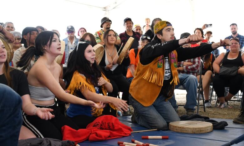 Three people kneel on the floor. On person is holds his arms straight out. 