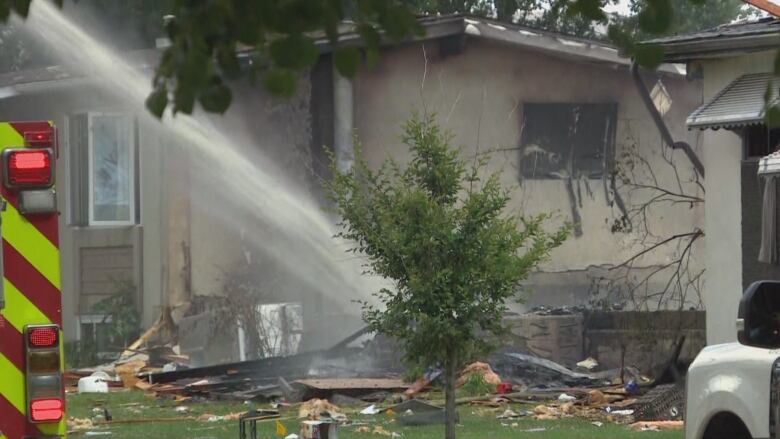 Water from a fire hose is sprayed onto a house foundation.